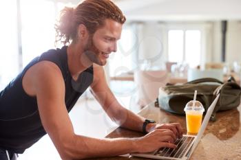 Millennial white man checking fitness app on laptop at home after a workout, side view