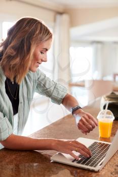 Millennial white woman checking fitness app on smartwatch and laptop at home after gym, vertical