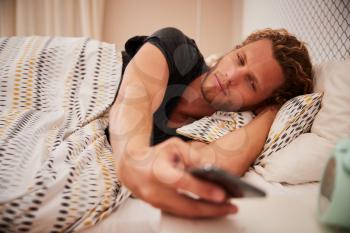 Millennial white man waking up in bad using smartphone, close up