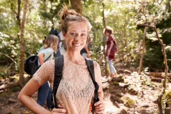 Portrait of millennial white woman with tied up hair hiking in a forest with her friends, close up