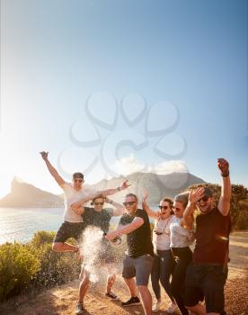 Six young adult  friends celebrating on a coastal path opening a bottle of champagne