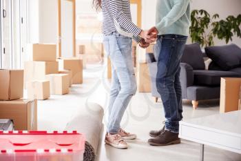Close Up Of Loving Couple Holding Hands Surrounded By Boxes In New Home On Moving Day