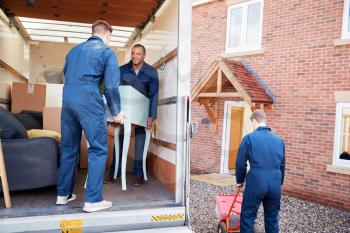 Removal Company Workers Unloading Furniture And Boxes From Truck Into New Home On Moving Day