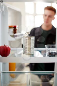 Young Man Looking Inside Refrigerator Empty Except For Open Tin Can On Shelf
