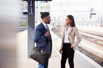 Businessman And Businesswoman Commuting To Work Talking On Railway Platform Waiting For Train
