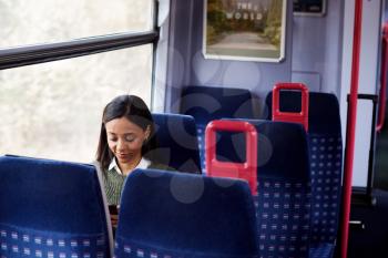 Female Passenger Sitting In Train Looking At Mobile Phone