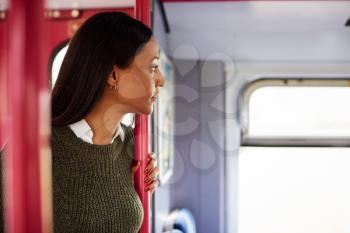 Female Passenger Standing By Doors In Train Looking Out Of Window