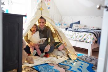Portrait Of Single Father Reading With Daughter In Den In Bedroom At Home
