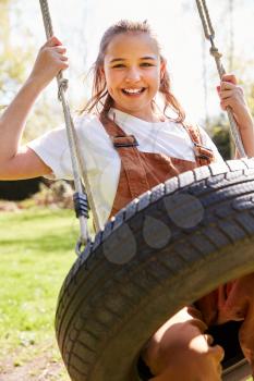 Portrait Of Girl Having Fun On Tyre Swing In Garden At Home