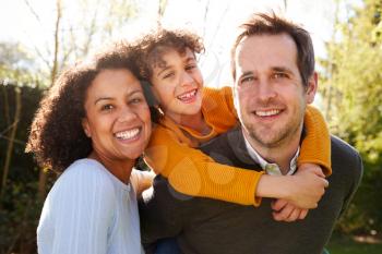 Outdoor Portrait Of Smiling Family In Garden At Home Against Flaring Sun