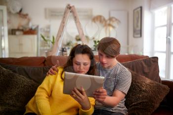 Young Downs Syndrome Couple Sitting On Sofa Using Digital Tablet At Home