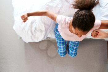 Overhead View Of Woman Wearing Pajamas Stretching As She Gets Out Of Bed At Home