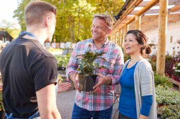 Mature Couple Buying Plants From Male Sales Assistant In Garden Center