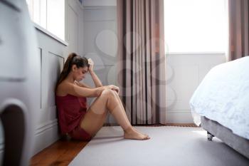 Depressed Woman Wearing Pajamas Sitting On Floor Of Bedroom