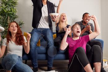 Group Of College Friends Celebrating Whilst Watching Sports Game On TV In Shared House