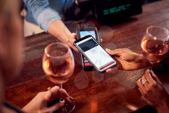 Close Up Of Woman Paying For Drinks At Bar Using Contactless App On Mobile Phone