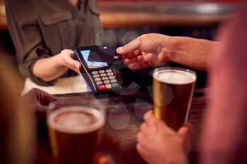 Close Up Of Man Paying For Drinks At Bar Using Contactless Card