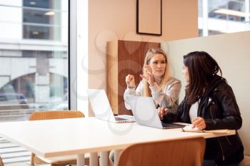Two Young Businesswomen In Meeting Around Table In Modern Open Plan Workspace