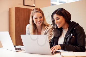 Two Young Businesswomen In Meeting Around Table In Modern Open Plan Workspace