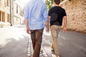 Rear View Of Male Gay Couple On Vacation Holding Hands Walking Along City Street