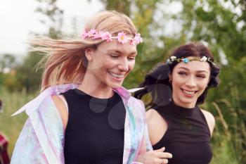 Two Excited Young Female Friends Arriving At Music Festival Walking Through Field