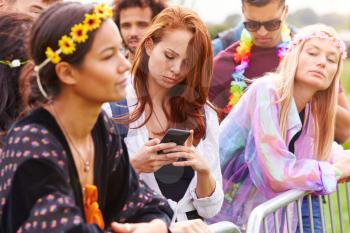 Young Woman Looking At Mobile Phone As She Waits Behind Barrier At Entrance To Music Festival Site