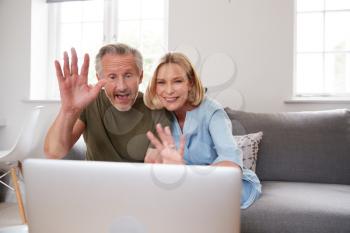 Senior Couple Sitting On Sofa At Home Making Video Call Using Laptop Computer Together