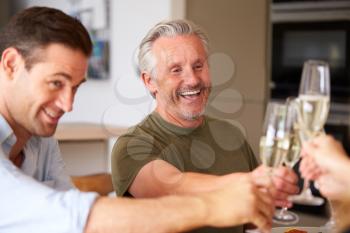 Family With Senior Parents And Adult Offspring Make A Toast Before Eating Meal Around Table At Home