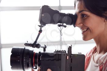 Female Videographer With Video Camera Filming Movie In White Studio