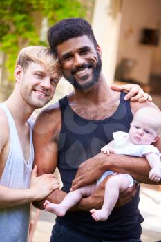 Portrait Of Loving Male Same Sex Couple Cuddling Baby Daughter At Home In Garden Together