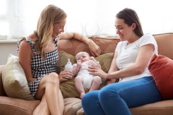 Loving Female Same Sex Couple Cuddling Baby Daughter On Sofa At Home Together