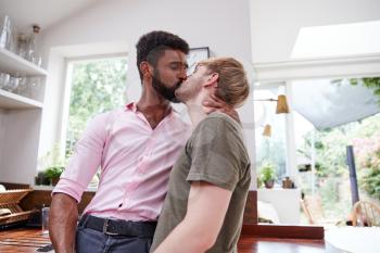 Loving Male Gay Couple Hugging And Kissing At Home In Kitchen