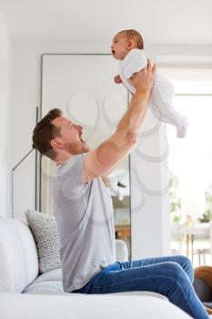 Loving Father Lifting 3 Month Old Baby Daughter In The Air In Lounge At Home