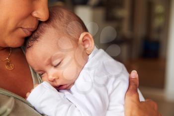 Close Up Of Loving Mother Holding Sleeping 3 Month Old Baby Daughter In Kitchen At Home