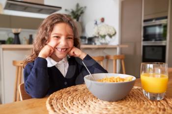 Portrait Of Girl Wearing Uniform In Kitchen Eating Breakfast Cereal Before Going To School