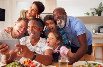 Multi-Generation Mixed Race Family Posing For Selfie As They Eat Meal Around Table At Home Together
