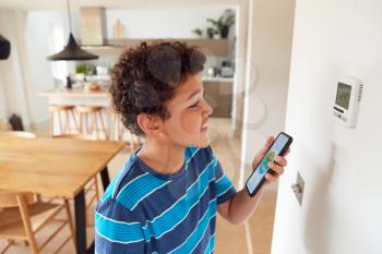 Boy Changes Temperature On Central Heating Thermostat Control Using Mobile Phone App
