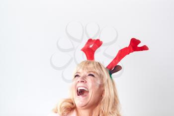 Studio Shot Of Laughing Mature Woman Wearing Dressing Up Reindeer Antlers Against White Background