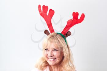 Studio Shot Of Happy Mature Woman Wearing Dressing Up Reindeer Antlers Against White Background