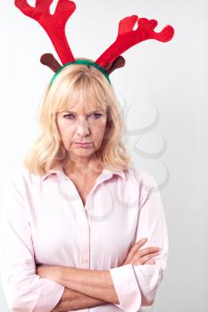 Studio Shot Of Unhappy Mature Woman Wearing Dressing Up Reindeer Antlers Against White Background