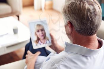 Mature Man Having Online Consultation With Female Doctor At Home On Digital Tablet