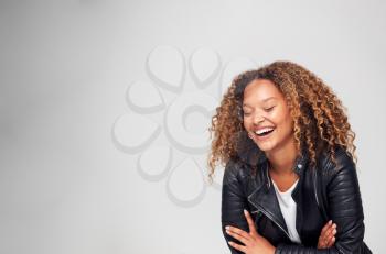Studio Shot Of Happy Young Woman With Folded Arms Wearing Leather Jacket Laughing Off Camera