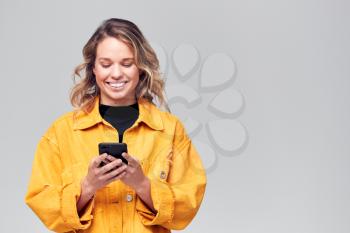 Studio Shot Of Smiling Causally Dressed Young Woman Using Mobile Phone