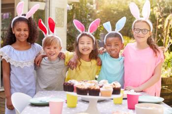 Portrait Of Children Wearing Bunny Ears Enjoying Outdoor Easter Party In Garden At Home
