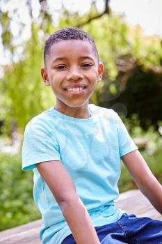 Portrait Of Smiling Boy Sitting On Wooden Table  In Garden