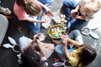Group Of Children Sitting On Floor At Home Eating Chocolate Eggs They Have Found On Easter Egg Hunt
