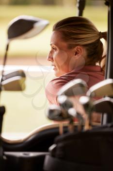 Rear View Of Mature Woman Playing Golf Driving Buggy Along Course Viewed Through Golf Clubs