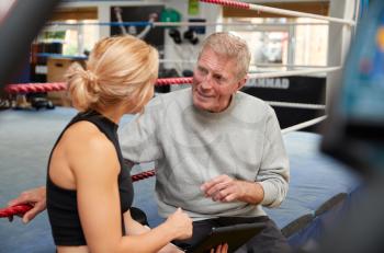 Female Personal Trainer With Senior Male Boxer In Gym Checking Performance Using Digital Tablet