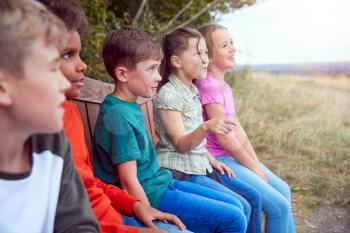 Group Of Children At Outdoor Activity Camp Resting On Bench During Walk Through Countryside