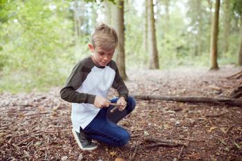 Boy On Outdoor Camping Trip In Forest Learning How To Make Fire By Rubbing Sticks Together